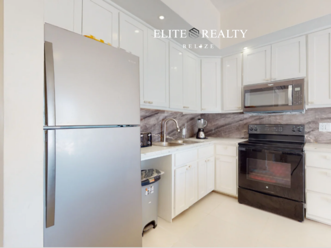 Modern kitchen with stainless steel refrigerator, stove, microwave, and cabinetry in beachfront condo at Blue Water Beach Resort Ambergris Caye Belize