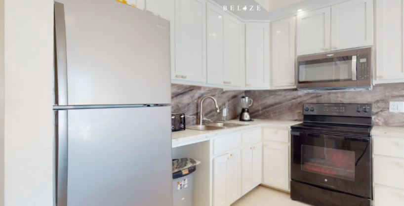 Modern kitchen with stainless steel refrigerator, stove, microwave, and cabinetry in beachfront condo at Blue Water Beach Resort Ambergris Caye Belize